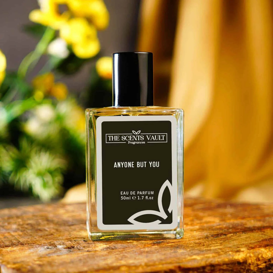 Anyone But You Eau de Parfum (50ml) from The Scents Vault, displayed against a background of yellow flowers and wooden surface.