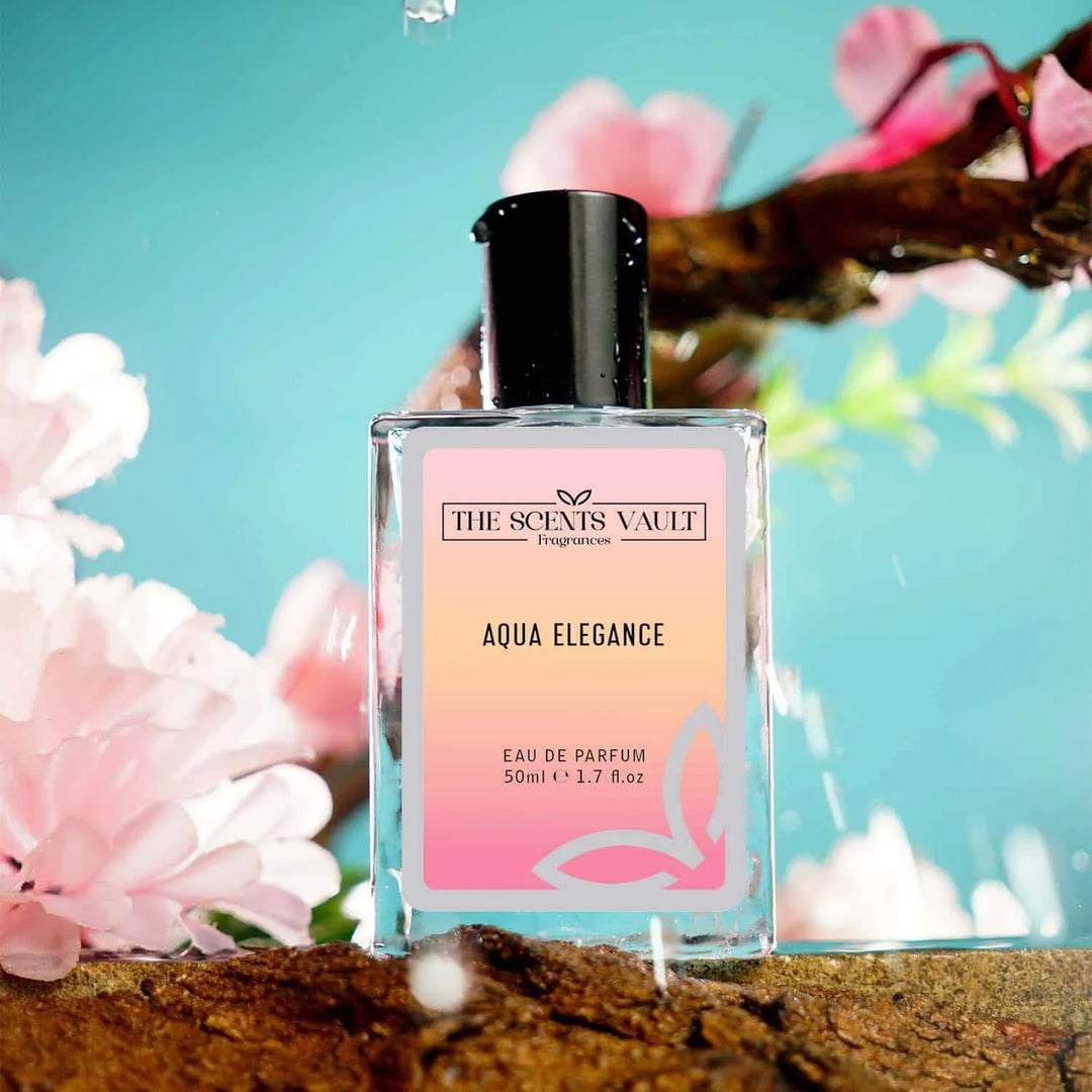 Aqua Elegance perfume by The Scents Vault placed on wet stone with pink cherry blossoms and splashing water.